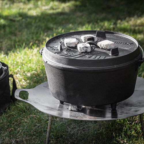 Heavy-duty cast iron pot with legs and a fitted lid holding charcoal briquettes on top, perfect for outdoor cooking and baking, featured in Kitchen & Food, Cookware, and Cast Iron collections.