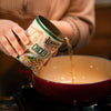 Hand pouring Lehman's canned chicken broth into a red pot, highlighting convenience for cooking stews, soups, and casseroles, ideal for kitchen, emergency supplies, and best sellers collections.