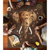 Group of four people assembling a 300-piece elephant-shaped jigsaw puzzle on a wooden table, with coffee, juice, colorful candy, and the puzzle box nearby in a family-friendly game setting.