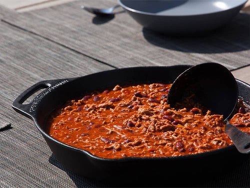 Cast iron skillet with a long handle and helper grip, filled with chili or stew, shown on an outdoor table, ideal for Farm, Garden & Tool, Camping, Kitchen & Food, and Cast Iron collections.
