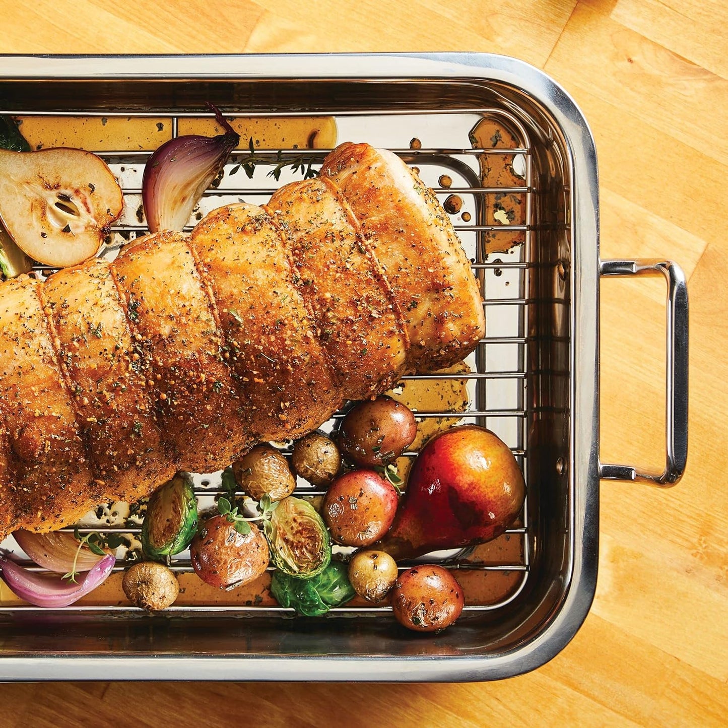 Stainless steel roasting pan with rack holding seasoned roast and roasted vegetables including potatoes, Brussels sprouts, onions, and a pear, part of Kitchen & Food and Cookware collections.