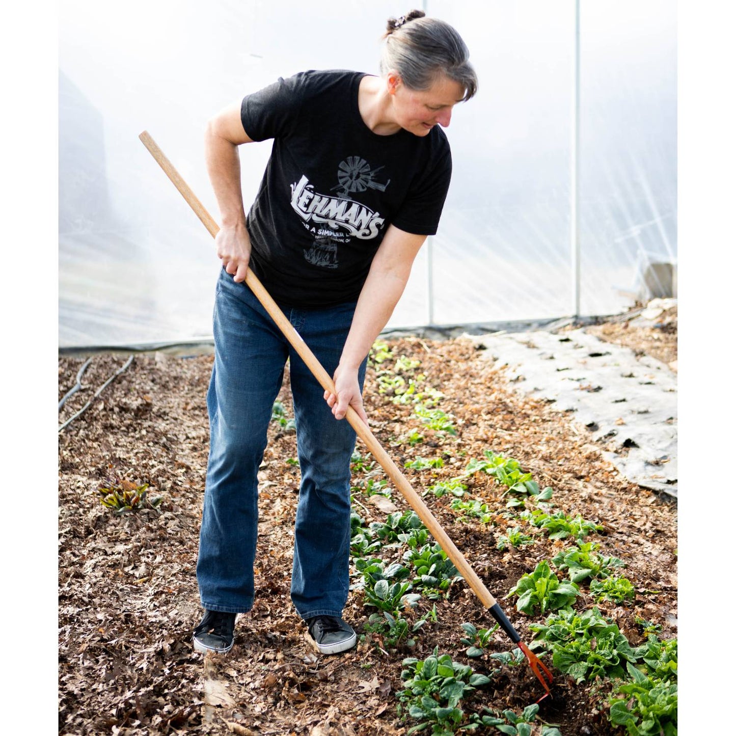 Woman using a handcrafted Amish made garden hoe with a wooden handle and hardened steel blade to cultivate soil in a greenhouse garden, USA made, best seller.