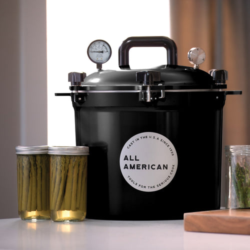 Black pressure canner with secure locking lid and pressure gauges, designed for safe food preservation in Kitchen & Food, Food Preservation, and USA Made collections, accompanied by jars of preserved asparagus.