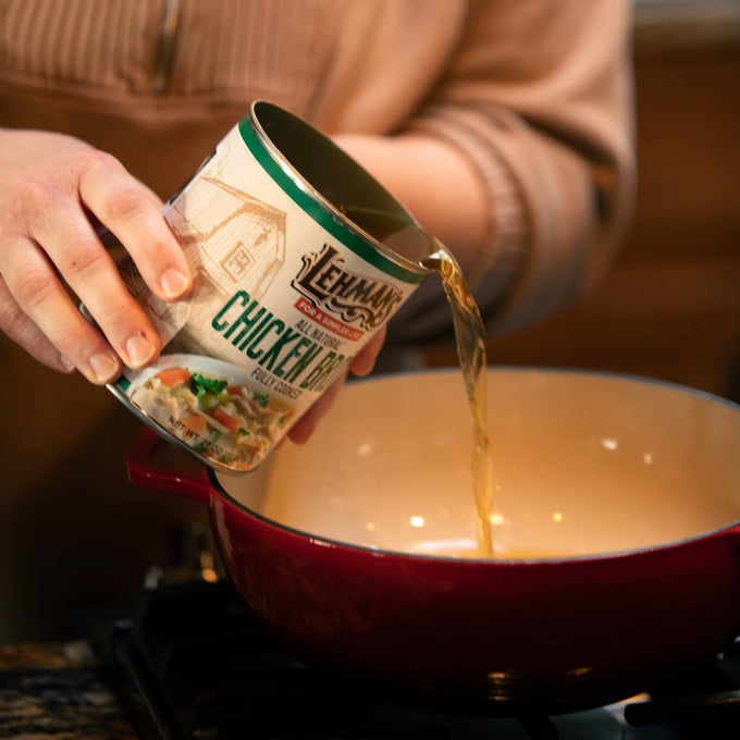 Hand pouring Lehman's canned chicken broth into a red cooking pot, illustrating ease of use for making soups, stews, and casseroles, featured in Farm, Kitchen & Food, and Emergency Supplies collections.