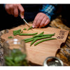 Handcrafted red alder cutting board with smooth finish and engraved logo, shown with hands slicing fresh green beans, ideal for Kitchen & Food and Food Prep collections.