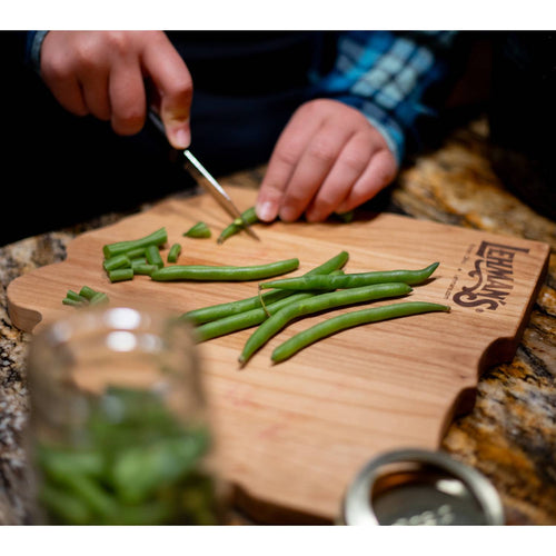 Handcrafted red alder cutting board with smooth finish and engraved logo, shown with hands slicing fresh green beans, ideal for Kitchen & Food and Food Prep collections.