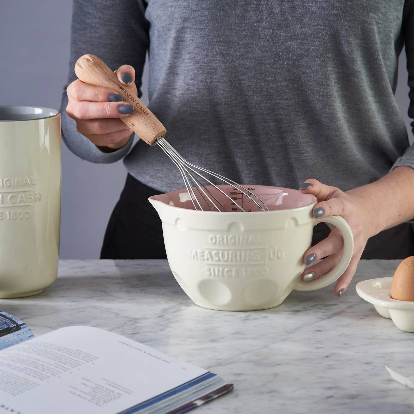 Person using a wooden-handled whisk to mix ingredients in a cream-colored Mason Cash measuring jug with a pink interior on a marble countertop, set among kitchenware in Kitchen & Food, Cookware, Baking Supplies, Food Prep, Measuring, Best Sellers, Promo Eligible collections.