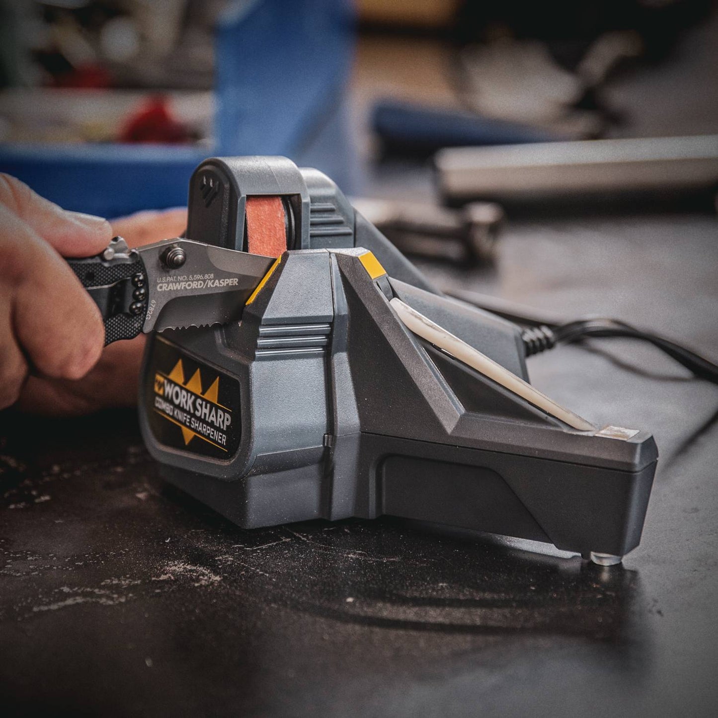 Person sharpening a serrated knife on a compact Work Sharp Combo Knife Sharpener with powered abrasive belt and manual ceramic honing rod, ideal for sharpening in Farm, Garden & Tool and Kitchen & Food collections.