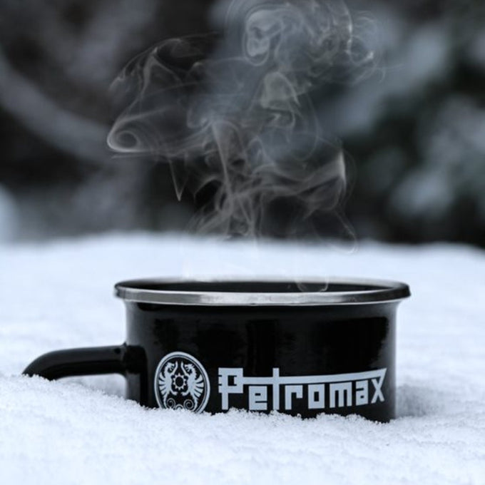 Black enameled steel Petromax mug with metal rim and bold white logo resting in snow with steam rising, suitable for Farm, Garden & Tool, Camping, Brewing Coffee and Tea, and Best Sellers collections.