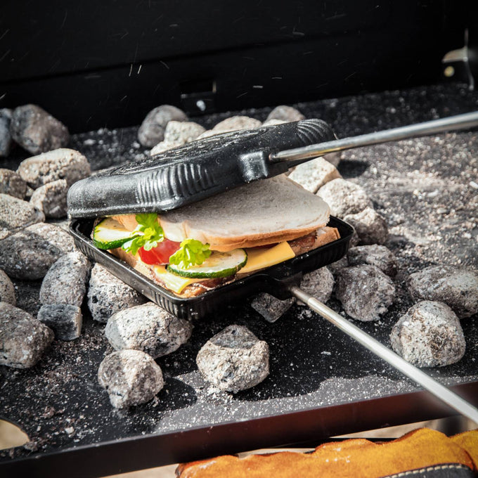 Cast iron sandwich iron with sandwich filled with cheese, vegetables, and meat being toasted over hot coals, designed for Camping, Farm, Garden & Tool, Best Sellers, and Promo Eligible collections.