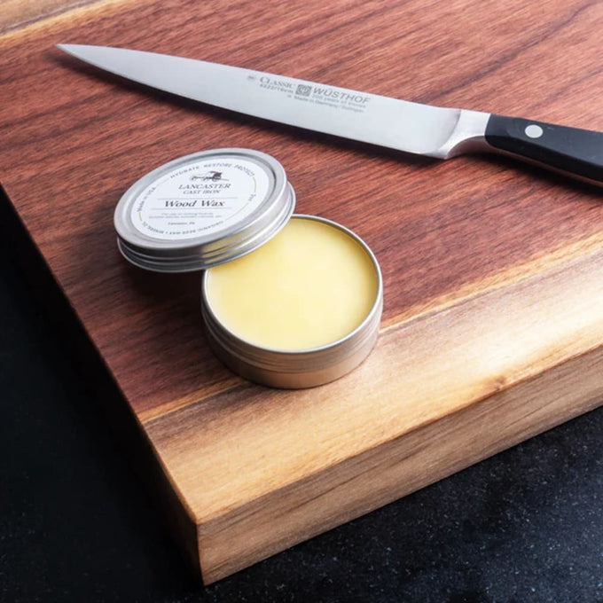 Open tin of Lancaster Wood Wax Conditioner with smooth yellow balm on a wooden cutting board next to a stainless steel kitchen knife, featured in Kitchen & Food and Food Prep collections.