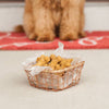 Wire basket lined with parchment paper filled with homemade dog bone treats, set on a floor mat with a blurred dog in the background, featured in Pet Supplies and Best Sellers collections.