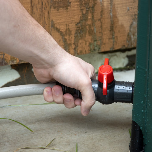 Hand turning the red valve handle on a black spigot connected to a garden water barrel, featured in Farm, Garden & Tool, Garden Accessories, Lawncare, Best Sellers, and Promo Eligible collections.