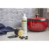 Biodegradable cleaner bottle, polycarbonate pan scraper, brush with stiff bristles, and black cleaning clips displayed on kitchen counter next to a red enameled cast iron pot, suitable for Cast Iron and Kitchen & Food collections.