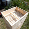 Handcrafted natural wood quilt box with ventilation screens and dovetail joinery, Amish made in the USA for moisture control in beekeeping, shown outdoors in garden setting.