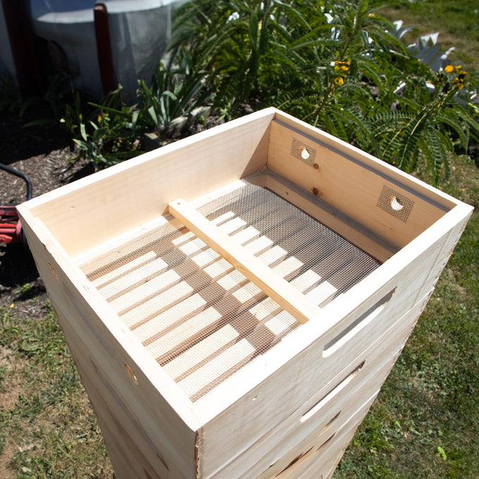 Handcrafted natural wood quilt box with ventilation screens and dovetail joinery, Amish made in the USA for moisture control in beekeeping, shown outdoors in garden setting.
