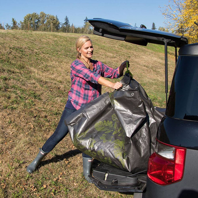 Woman using reinforced woven polyethylene tarp with soft grip handles to load yard debris into a vehicle, ideal for Farm, Garden & Tool and Lawncare collections.