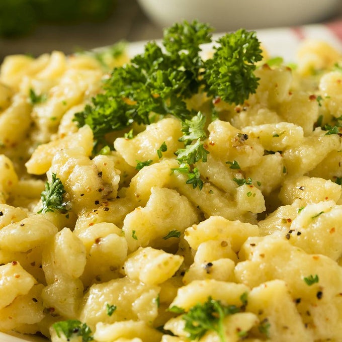 Close-up of golden spaetzle noodles tossed with herbs and freshly cracked black pepper, garnished with vibrant parsley, perfect for Kitchen & Food, Cookware, and Best Sellers collections.