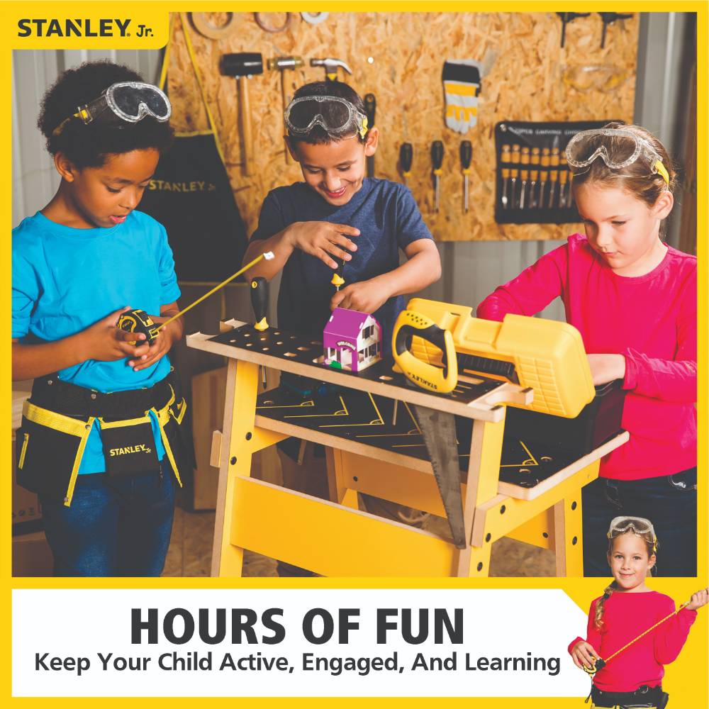 Three children wearing safety goggles use a children’s workbench and real tools including a saw and tape measure, engaging in hands-on indoor play and learning activities.