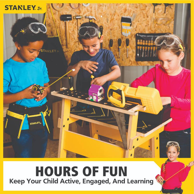 Three children wearing safety goggles use a children’s workbench and real tools including a saw and tape measure, engaging in hands-on indoor play and learning activities.