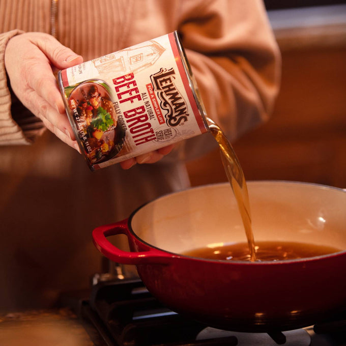Person pouring rich amber-colored beef broth from a can into a red enameled pot on a stovetop, highlighting a convenient pantry staple for Farm, Garden & Tool, Kitchen & Food, Emergency Supplies, Food, Meats, Best Sellers, and Promo Eligible collections.