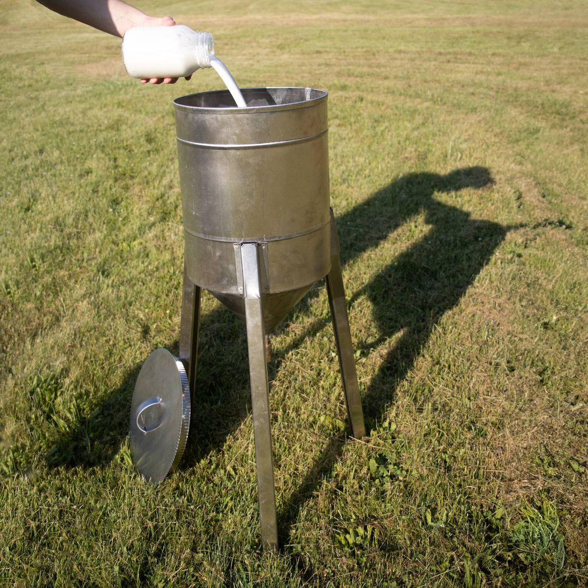 Handcrafted rust-proof stainless steel cream separator with three-leg stand on grass, milk being poured in, ideal for farm, garden, and animal care, made in USA collections.