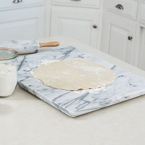 Smooth marble board with rounded edges and rubber feet, being used to roll out dough in a bright kitchen, featured in Kitchen & Food, Cookware, Baking Supplies, and Holiday Hosting collections.