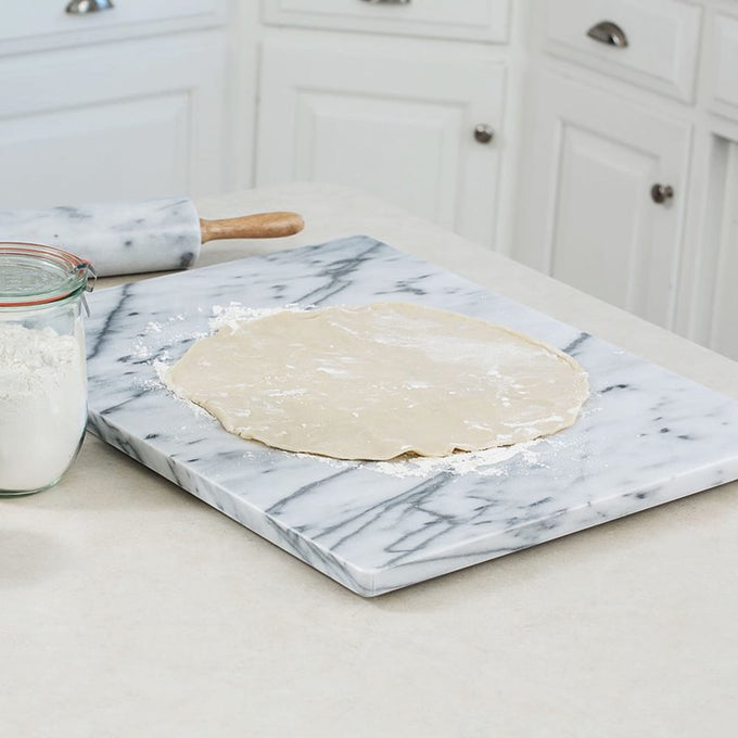 Smooth marble board with rounded edges and rubber feet, being used to roll out dough in a bright kitchen, featured in Kitchen & Food, Cookware, Baking Supplies, and Holiday Hosting collections.