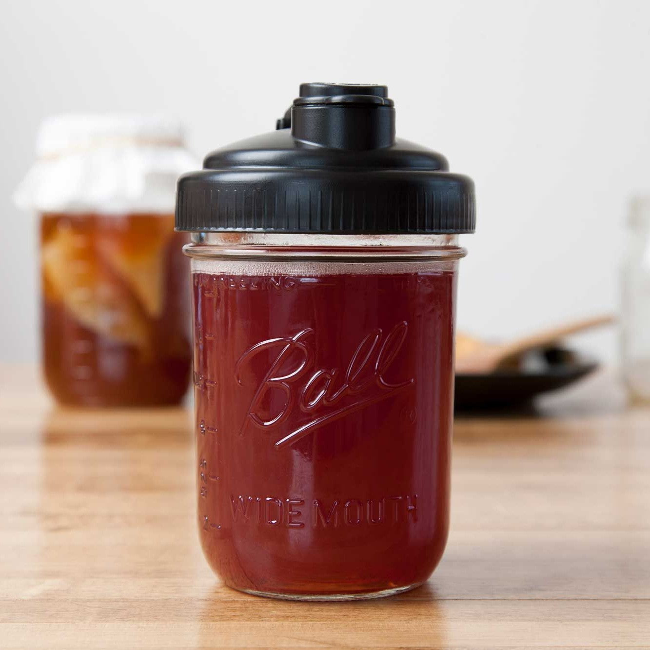 Clear glass wide-mouth mason jar filled with dark liquid, topped with a black pour lid featuring a flip-top spout and carry loop, crafted from durable no-break plastic and made in USA, suitable for Kitchen & Food, Dinnerware, Kitchen Gadgets, Kitchen Accessories, USA Made, Best Sellers, and Promo Eligible collections.
