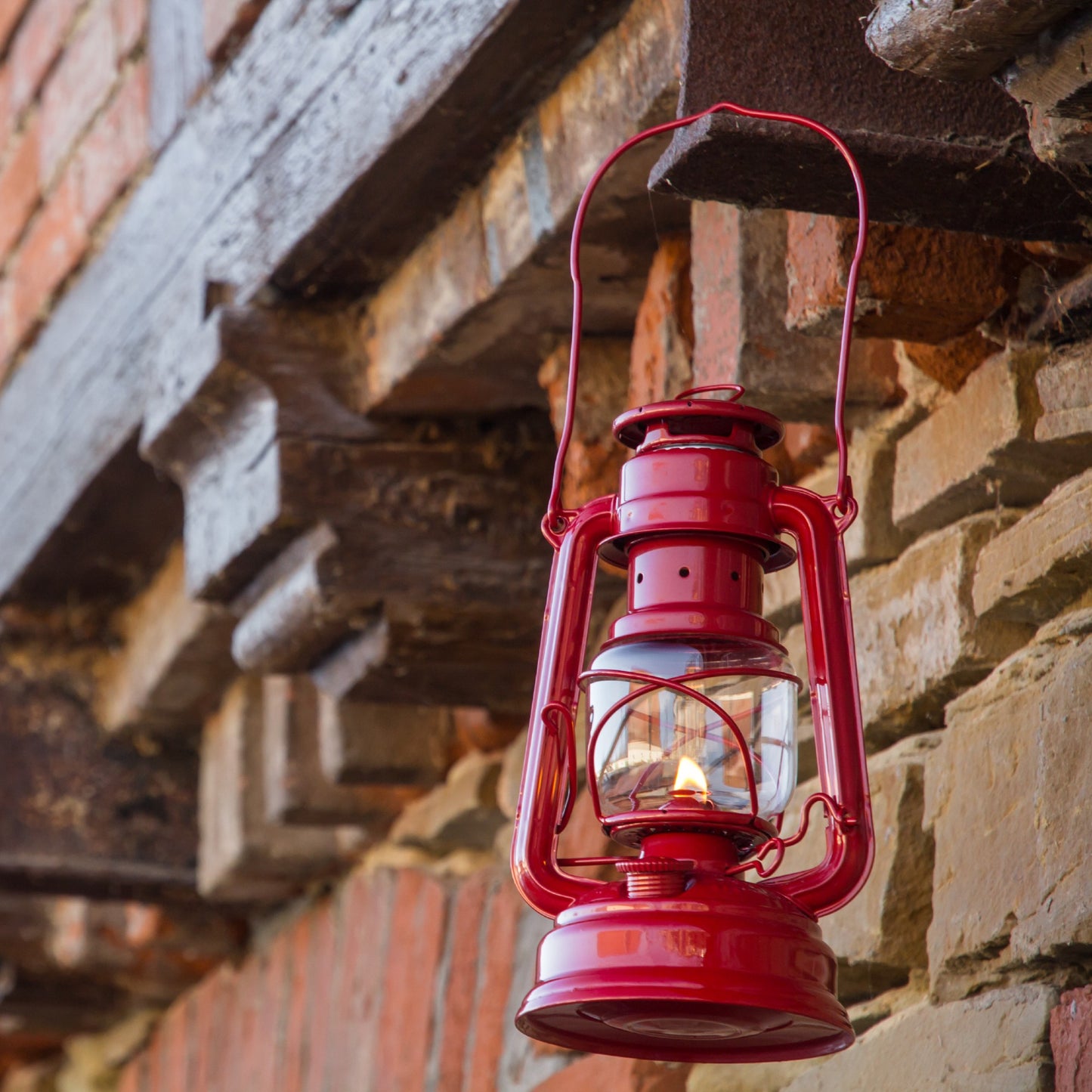 Handcrafted bright red galvanized oil lantern with thermal heat-resistant SUPRAX globe burning outdoors against rustic brick, perfect for Lamps & Lighting, Camping, Emergency Supplies collections.