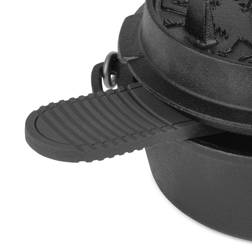 Close-up of a black silicone trivet inserted under the handle of a cast iron Dutch oven lid, designed to protect surfaces and provide a non-slip grip, ideal for farm, kitchen, camping, and cookware use.