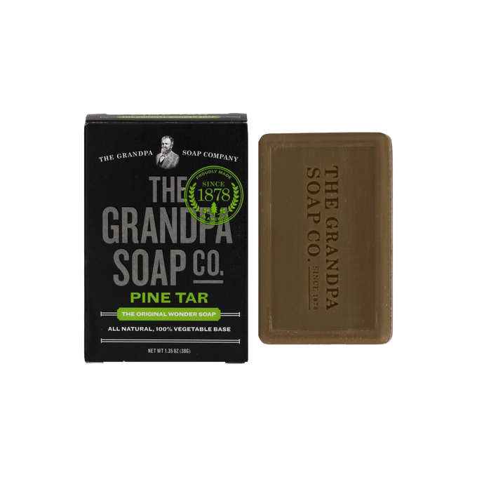 Bar of pine tar soap with embossed logo beside black box featuring vintage-style branding and green seal, natural and vegetable-based, part of Health & Wellness, Soaps, and USA Made collections.