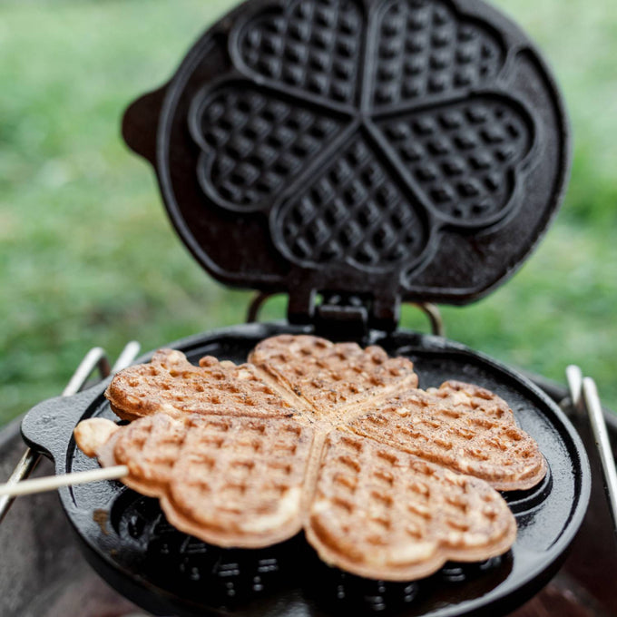 Handcrafted cast iron rotating waffle iron with five heart-shaped waffle segments cooking over an outdoor campfire, perfect for Farm, Garden & Tool, Camping, and Best Sellers collections.