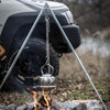 Adjustable metal tripod with hanging chain supporting a kettle over an open campfire, set outdoors near a vehicle, ideal for Farm, Garden & Tool, Camping, Best Sellers, and Promo Eligible collections.
