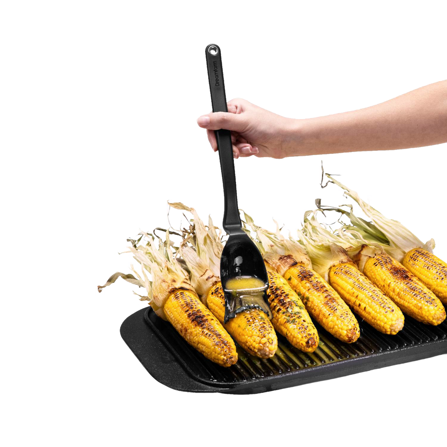 Hand using a flexible black basting brush with a deep scooping head to glaze charred corn on the cob on a ridged grill pan, ideal for Kitchen & Food and Grilling collections.