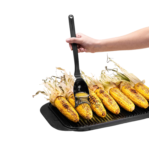 Hand using a flexible black basting brush with a deep scooping head to glaze charred corn on the cob on a ridged grill pan, ideal for Kitchen & Food and Grilling collections.