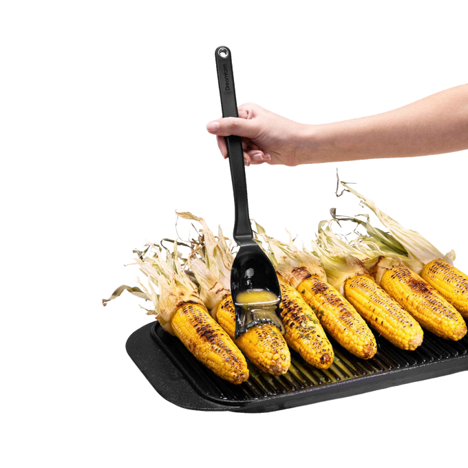 Hand using a flexible black basting brush with a deep scooping head to glaze charred corn on the cob on a ridged grill pan, ideal for Kitchen & Food and Grilling collections.