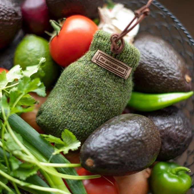 Olive green natural wool ripening sock with leather loop and label, sized to hold one avocado, surrounded by fresh produce, featured in Kitchen & Food and Best Sellers collections.