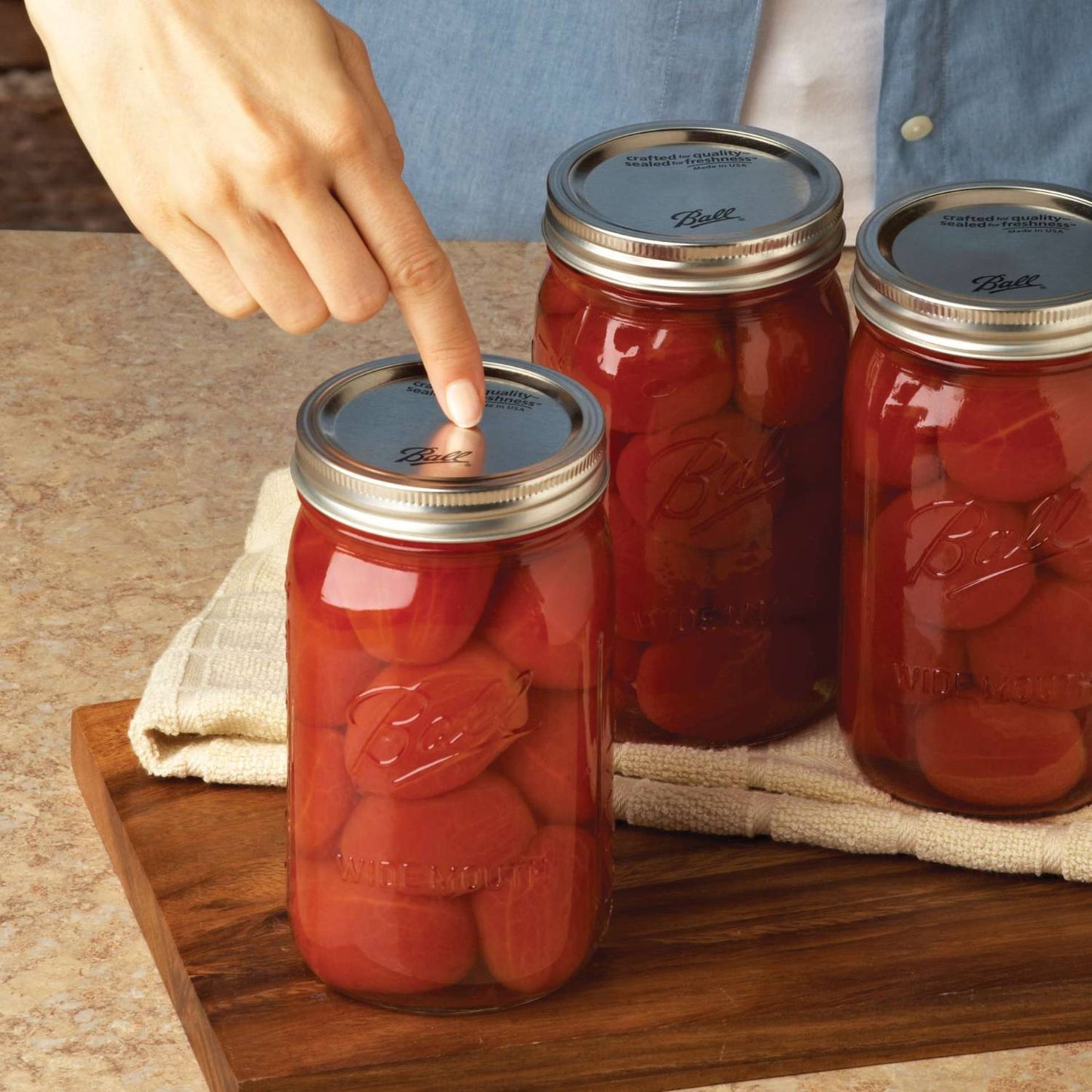 Hand pressing silver single-seal lid on a glass jar of preserved tomatoes, showcasing reliable BPA-free lids made in USA, featured in Kitchen & Food and Food Preservation collections.