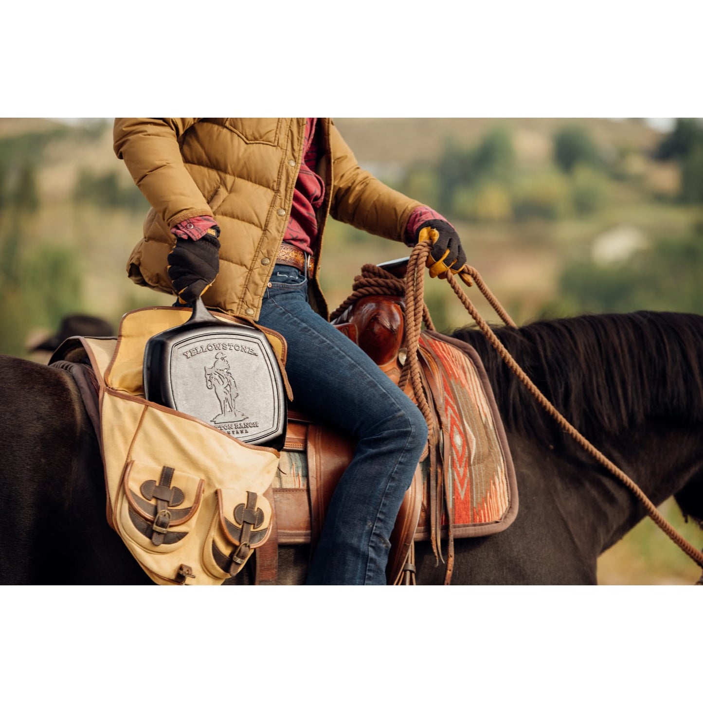 Handcrafted cast iron square grill pan with seasoned ribs, held in a leather bag by a rider wearing gloves and casual outdoor clothing, set on a horseback in a natural landscape, ideal for Kitchen & Food, Cookware, Cast Iron, and USA Made collections.