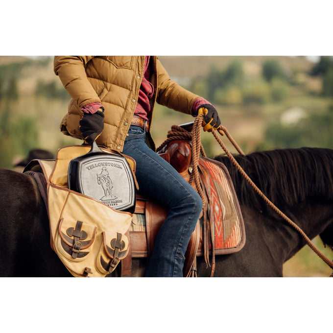 Handcrafted cast iron square grill pan with seasoned ribs, held in a leather bag by a rider wearing gloves and casual outdoor clothing, set on a horseback in a natural landscape, ideal for Kitchen & Food, Cookware, Cast Iron, and USA Made collections.