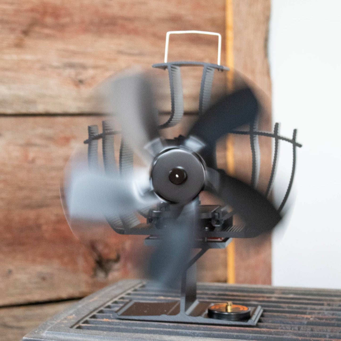 Black handcrafted oscillating stove fan with curved blades spinning on a wood-burning stove, designed to improve air circulation in stoves and hearth accessories collections.
