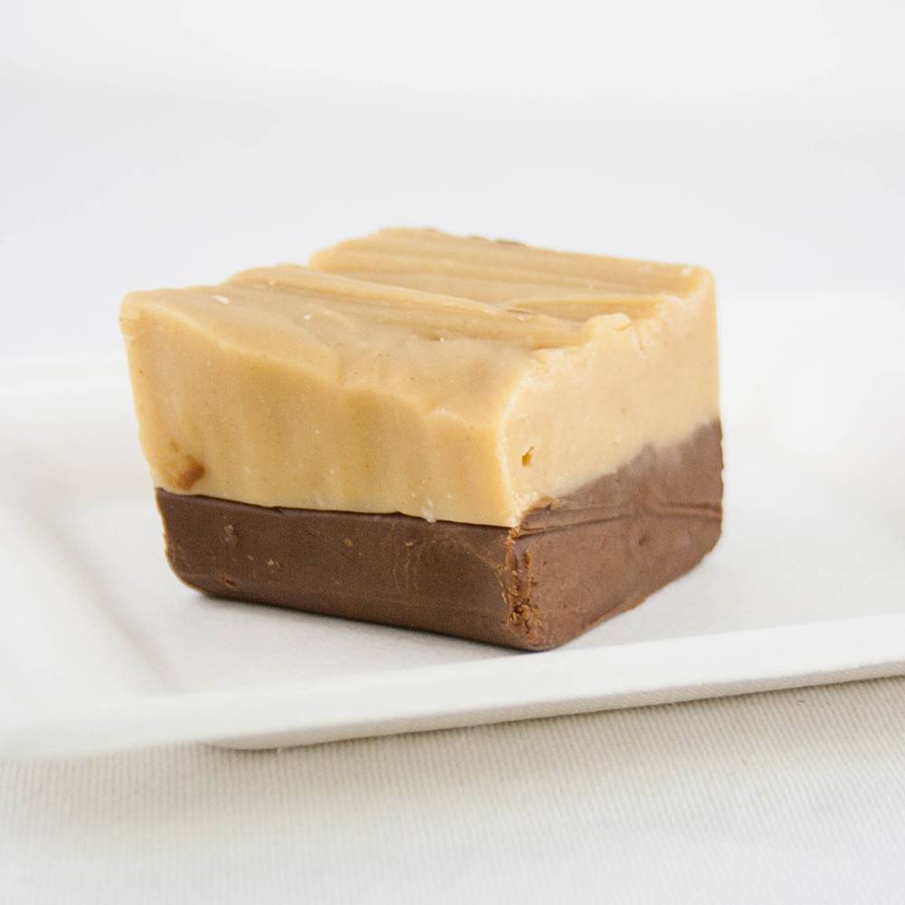 Single handcrafted two-layer fudge piece with creamy caramel top and rich chocolate bottom on a white plate, featured in Kitchen & Food, Food, Snacks and Sweets, USA Made, Best Sellers, and Promo Eligible collections.