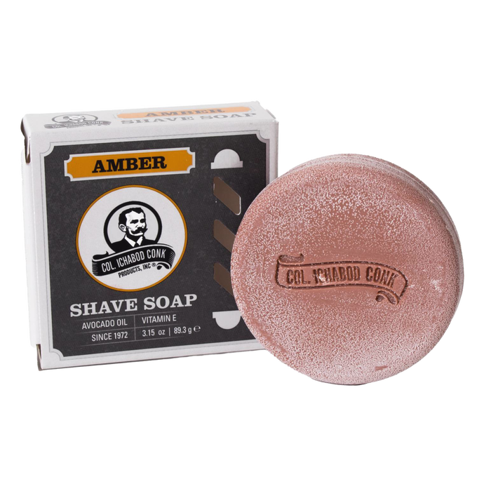 Round amber-colored shaving soap bar with embossed branding beside its box, containing avocado oil and vitamin E, crafted in USA, featured in Health & Wellness and Grooming collections.