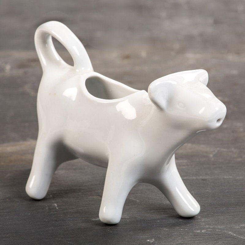 White porcelain cow-shaped creamer with a tail handle and spout mouth, handcrafted and microwave, oven, and dishwasher safe, ideal for Kitchen & Food and Dinnerware collections.