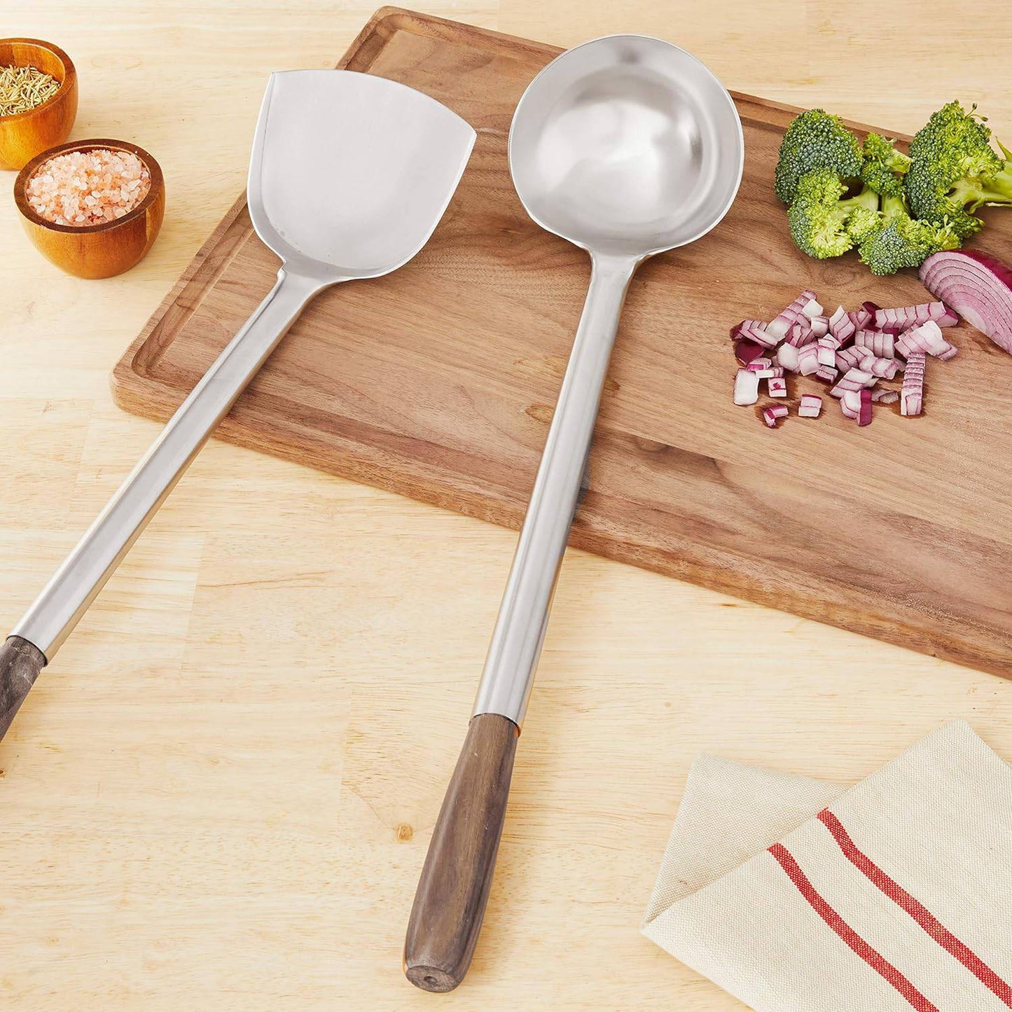 Set of two stainless steel wok utensils with wooden handles, featuring a spatula and ladle, displayed on a wooden cutting board with chopped vegetables, ideal for Kitchen & Food and Kitchen Gadgets collections.