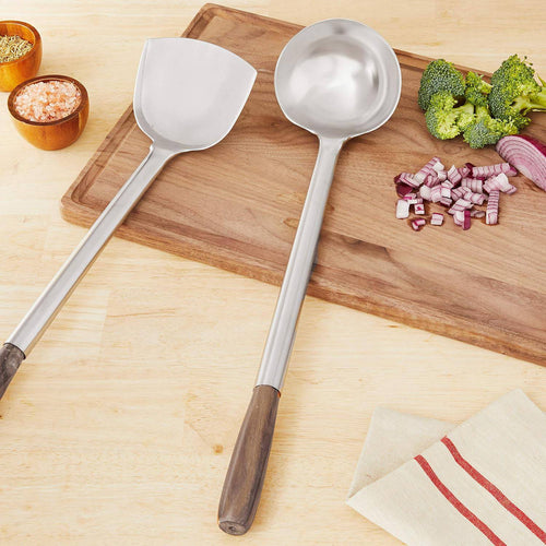 Set of two stainless steel wok utensils with wooden handles, featuring a spatula and ladle, displayed on a wooden cutting board with chopped vegetables, ideal for Kitchen & Food and Kitchen Gadgets collections.