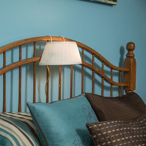 White pleated shade lamp hanging from wooden headboard with a pull chain switch, providing convenient bedside lighting for reading, featured in Home & Decor and Lamps & Lighting collections.