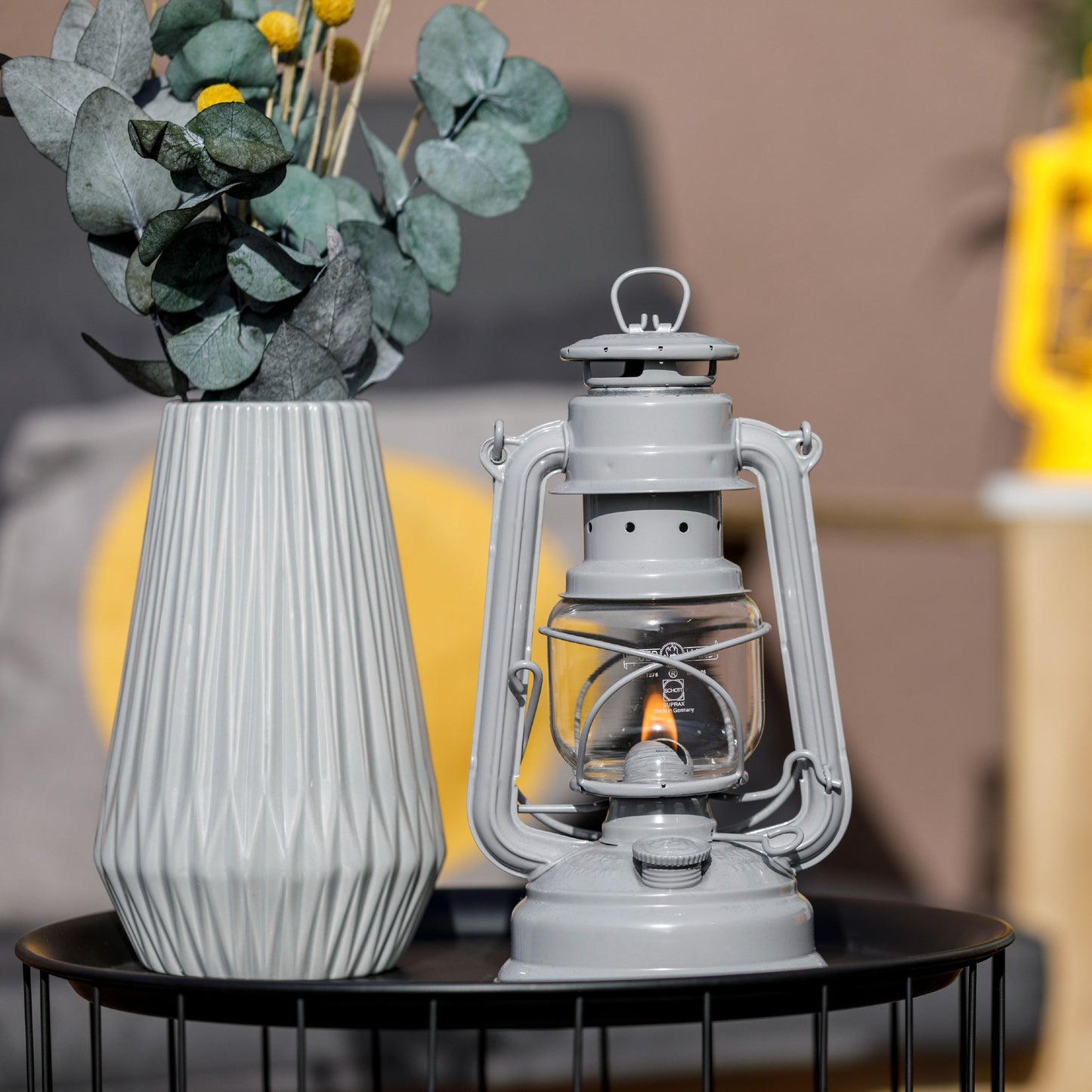 Handcrafted light gray galvanized oil lantern with a glowing thermal heat-resistant SUPRAX globe, displayed on a black wire table next to a textured ceramic vase and greenery, ideal for Lamps & Lighting, Camping, and Emergency Supplies collections.