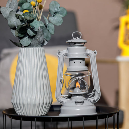 Handcrafted light gray galvanized oil lantern with a glowing thermal heat-resistant SUPRAX globe, displayed on a black wire table next to a textured ceramic vase and greenery, ideal for Lamps & Lighting, Camping, and Emergency Supplies collections.